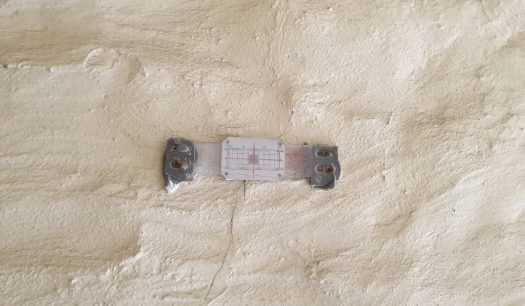 Cracks in walls being tracked with a crack monitor fixed across a crack in a UK building